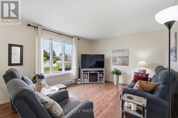 Living room with two grey chairs, a sofa, hardwood floors, and a large window overlooking the street. - 353 Nelson Street E, Hawkesbury