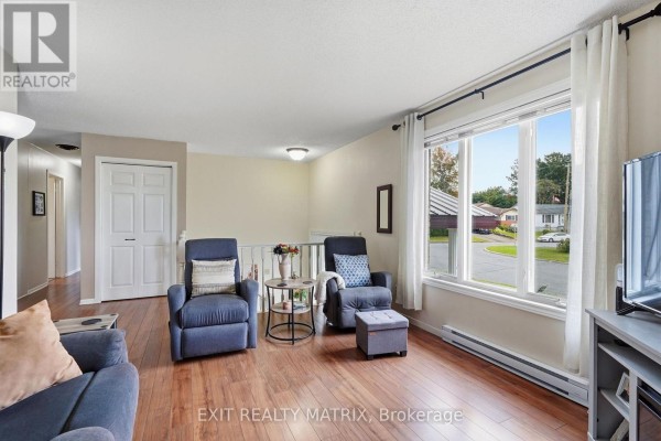 Living room with two blue recliners, a sofa, hardwood floors, and a large window with a view of the neighborhood. - 353 Nelson Street E, Hawkesbury