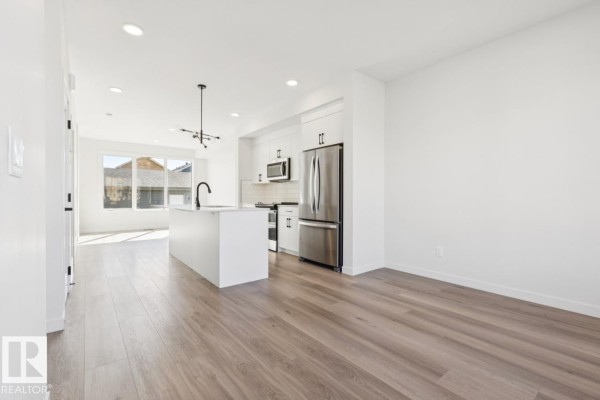 Open concept living and kitchen area with white island, stainless steel appliances, and large windows. - 353 Rankin Dr, St  Albert
