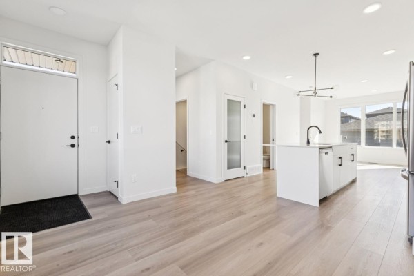 View of the open-concept living area, kitchen island, and front entryway with white walls and light floors. - 353 Rankin Dr, St  Albert