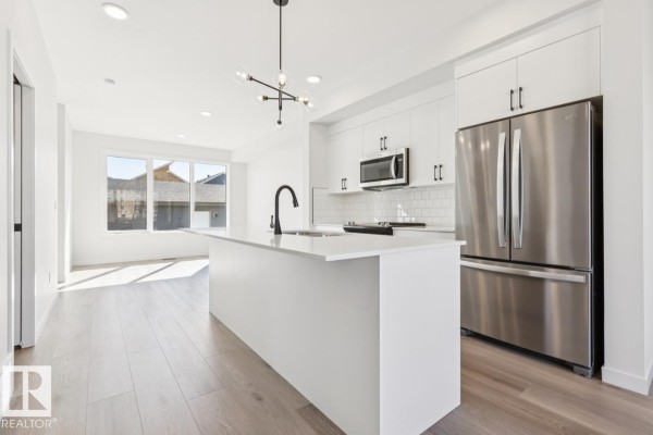 Kitchen and dining area with white island, stainless steel refrigerator and oven, and large windows. - 353 Rankin Dr, St  Albert