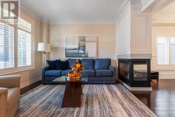 Living room with a blue sofa, fireplace, large windows with shutters, and a glass coffee table. - 353 Shipway Avenue, Clarington