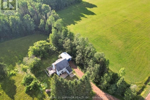 Overhead view of the property with the white farmhouse, detached garage, and surrounding woodland. - 353 Spring Creek Drive, Dorion