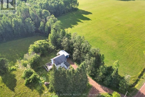Drone shot of the farmhouse and its expansive natural surroundings, including fields and mature trees. - 353 Spring Creek Drive, Dorion
