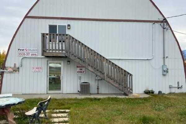 Wooden stairs lead to a glass door and window on the side of a Quonset building. - 3531 37 Avenue, Whitecourt