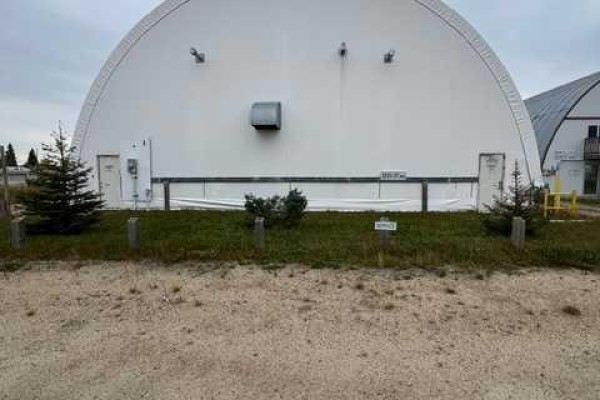 Front view of a large white Quonset building with two doors and two small evergreen trees. - 3531 37 Avenue, Whitecourt