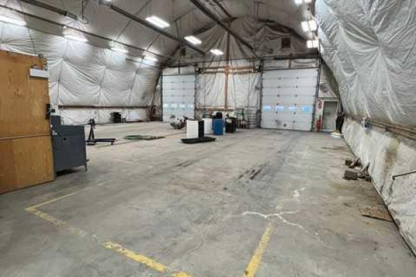 Interior of a large Quonset building with a concrete floor, three garage doors, and overhead lighting. - 3531 37 Avenue, Whitecourt