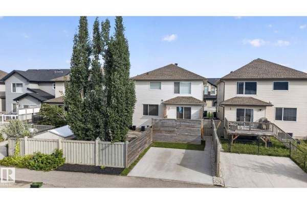 Backyard view of three houses with wooden fences, decks, and paved driveways. - 3536 Claxton Cr Sw Sw, Edmonton