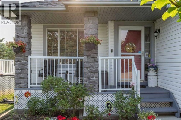 Covered front porch with stone columns, white railing, and stairs leading to the red front door. - 354 West Creek Springs, Chestermere