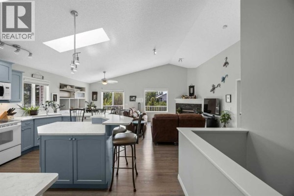Open-concept kitchen and living room with blue cabinets, an island, vaulted ceiling, and fireplace. - 354 West Creek Springs, Chestermere