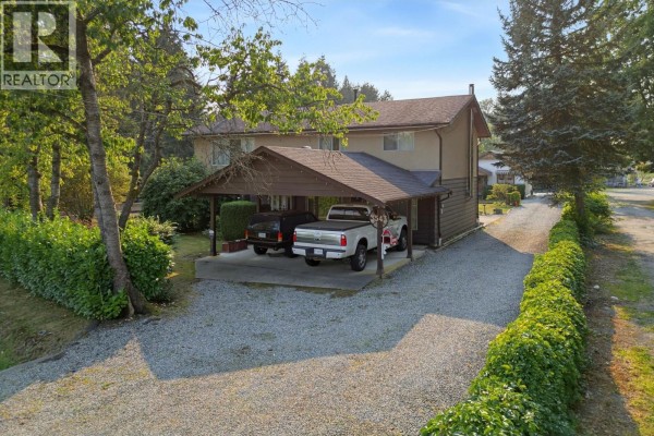 Covered carport with two vehicles parked underneath, adjacent to a two-story house. - 3543 Devon Road, Port Coquitlam