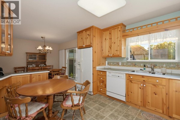 Kitchen area with wooden cabinets, a round table, chairs, and a dining room view. - 3543 Devon Road, Port Coquitlam
