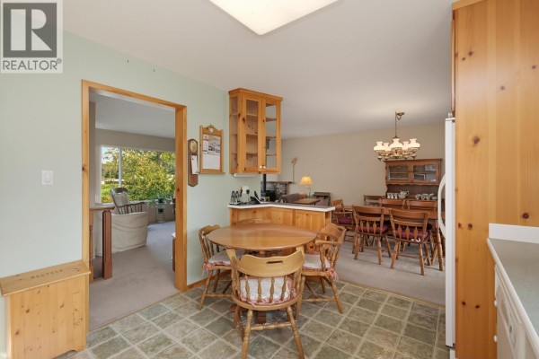 Kitchen and dining area showing wooden cabinets, tables, chairs, and an entryway. - 3543 Devon Road, Port Coquitlam