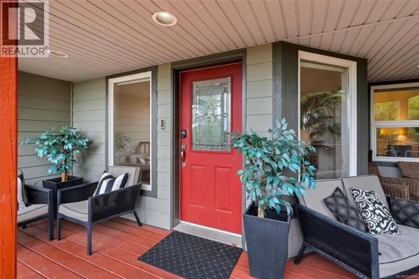Front door area with a red door, seating, and potted plants on a wooden deck. - 3549 Sun Estate, Langford