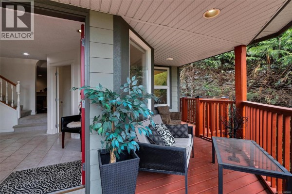 Covered front porch with seating, potted plants, and a table overlooking a wooded area. - 3549 Sun Estate, Langford