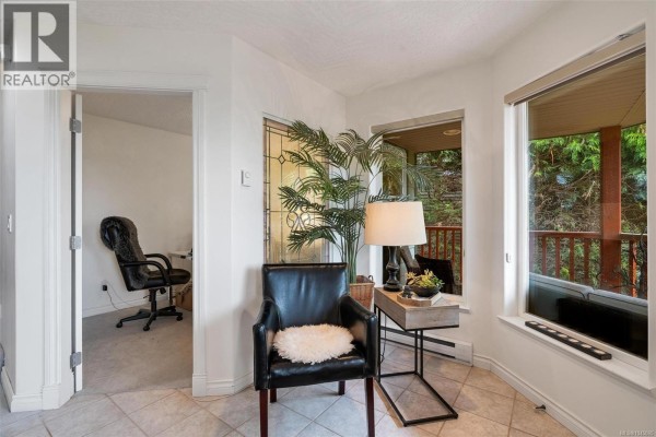 A windowed room with a black leather chair, side table, lamp, and view of the outdoors. - 3549 Sun Estate, Langford