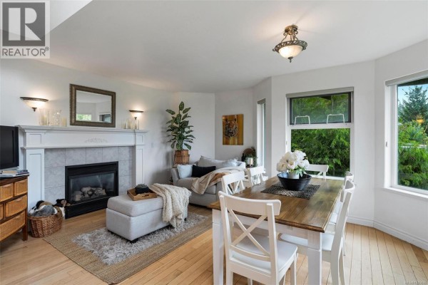 Living and dining area with a fireplace, sofa, dining table, chairs, and large windows. - 3549 Sun Estate, Langford