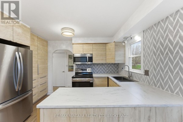 Modern U-shaped kitchen with light wood cabinets, stainless steel appliances, and marble countertops. - 355 Bernard Avenue, Fort Erie