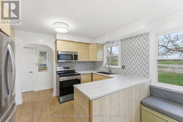 Kitchen with light wood cabinets, stainless steel appliances, grey patterned backsplash, and window seating. - 355 Bernard Avenue, Fort Erie