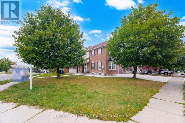 Side view of a brick townhouse complex with green trees in the foreground. - 355 Brisdale Drive, Brampton