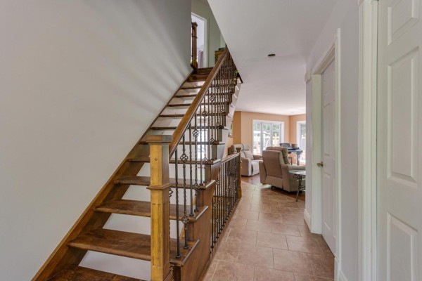 Interior hallway with a wooden staircase featuring ornate metal railings and tiled flooring. - 355 Ch. St-antoine, Val Des Monts