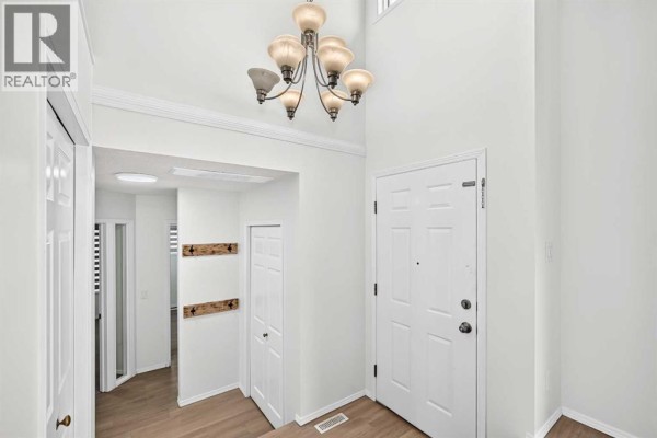 Interior entryway with white double doors, a large chandelier, and light wood floors. - 355 Millrise Drive Sw, Calgary