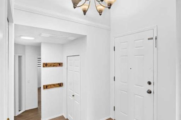 Interior entryway with white double doors, a large chandelier, and light wood floors. - 355 Millrise Drive Sw, Calgary