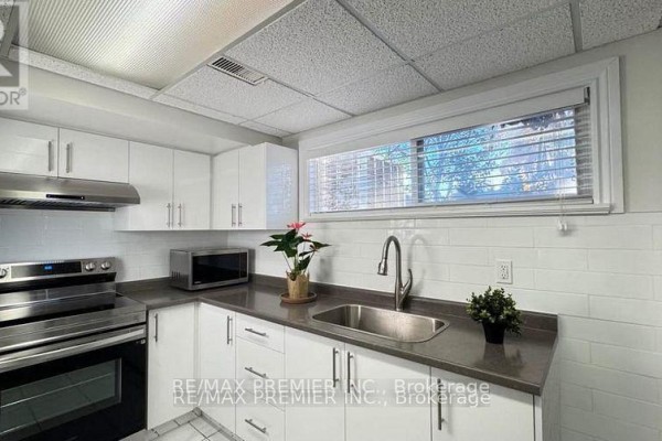 A laundry area with stacked washer and dryer, stainless steel refrigerator, and sink. - 3551 Burningelm Crescent, Mississauga