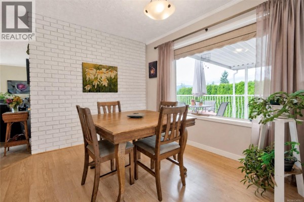 Dining room with wood table, chairs, brick accent wall, and a large window. - 356 Rees Rd, Courtenay