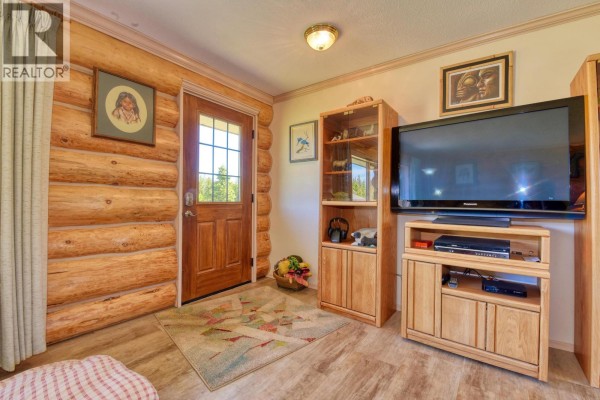 Entryway with a wood door, log walls, a television, entertainment center, and shelving unit. - 3574 Spokin Lake Road, Williams Lake