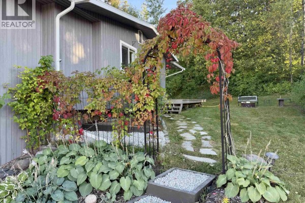 Wooden deck with a glass table and four chairs, overlooking a grassy yard with a shed. - 358 W 5th Street, Vanderhoof