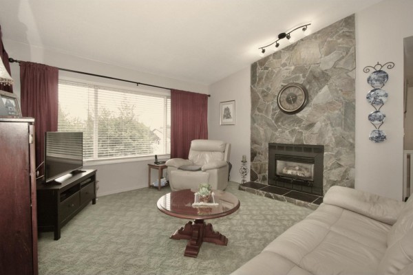 Living room with a stone fireplace, beige sofa, recliner, and dark wood entertainment unit. - 35807 Sunridge Place, Abbotsford