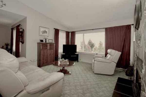 Living room featuring a large stone fireplace, beige sofa, recliner, and floor-to-ceiling window. - 35807 Sunridge Place, Abbotsford