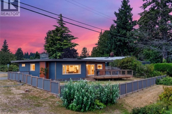 Rancher exterior at dusk with warm interior lights glowing and a vibrant pink and purple sunset sky. - 3584 Island Hwy, Campbell River