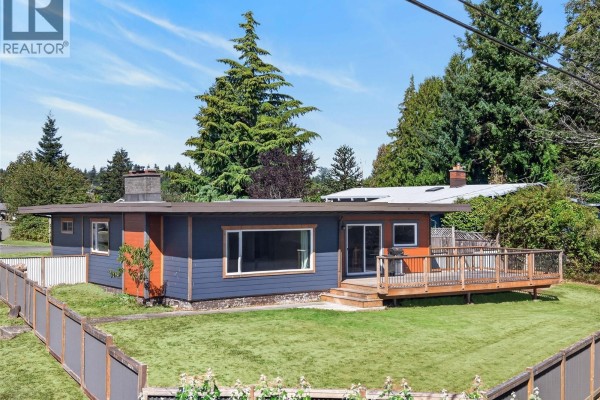 Side view of the ranch-style house showing a grass lawn, wooden fence, and large windows. - 3584 Island Hwy, Campbell River