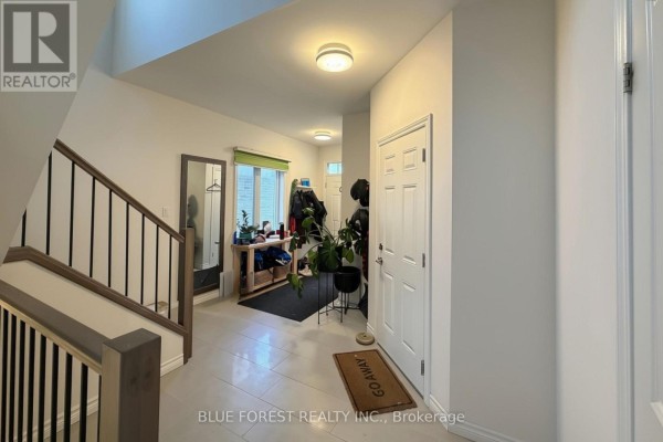 Hallway with beige tile flooring, a staircase with black spindles, and a front door. - 3584 Singleton Avenue, London South
