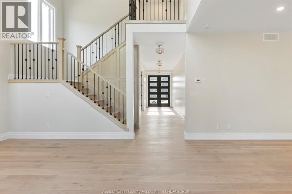 Spacious foyer with a grand staircase featuring wood treads and black metal railings, leading to a hallway with a glass front door. - 3586 Sutton Avenue, Windsor