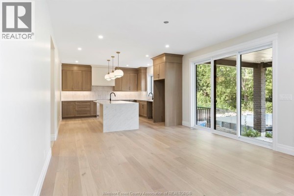 Open-concept kitchen and living area with light wood cabinets, a large white marble island, and sliding glass doors leading outdoors. - 3586 Sutton Avenue, Windsor