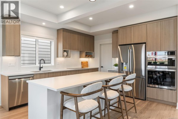 View of the modern kitchen island, dining area, and abstract artwork. - 3587 Temperate Pl, Colwood