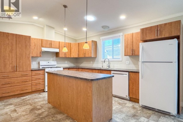 A bright kitchen with light wood cabinets, a white gas stove, dishwasher, and island. - 3591 Old Vernon Road Unit# 110b, Kelowna