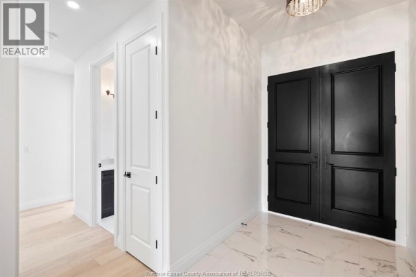Interior hallway with white walls, wood floors, and black double doors. - 3592 Sutton Avenue, Windsor