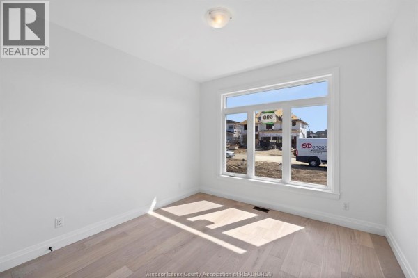 Empty room with white walls, wood floors, and a large picture window overlooking construction. - 3592 Sutton Avenue, Windsor