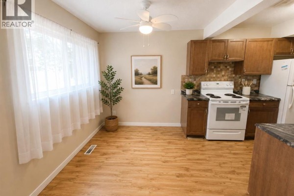 Kitchen and dining area with light wood laminate flooring, white appliances, and dark wood cabinets. - 36, 55 Lemoyne Crescent W, Lethbridge