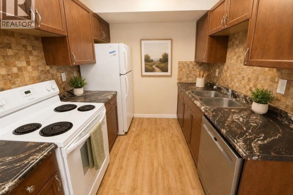 Narrow kitchen with dark granite countertops, light wood laminate flooring, and white appliances. - 36, 55 Lemoyne Crescent W, Lethbridge
