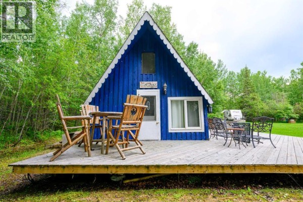 Wooden chairs and table set on a deck in front of the blue A-frame cabin entrance. - 36, 70544 243 Range, Rural Greenview No  16, M D  Of
