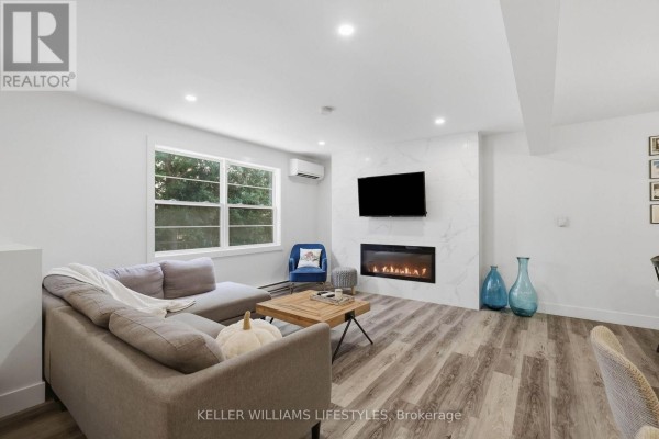 Living room with grey sectional sofa, electric fireplace, television, and wood plank flooring. - 36 - 105 Andover Drive, London South