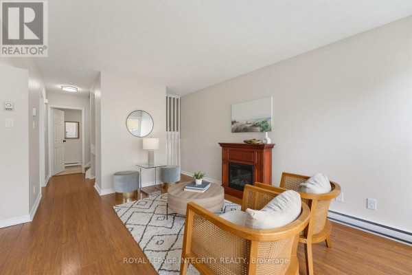 Living room with fireplace, two chairs, rug, and hallway leading to bedrooms. - 36 - 3415 Uplands Drive, Ottawa