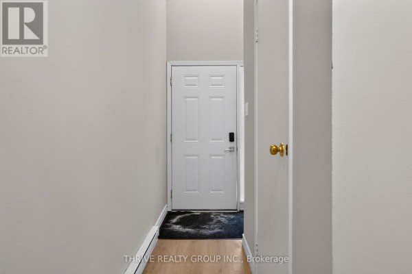 Hallway with a white front door, beige walls, and light wood laminate flooring. - 36 - 40 Summit Avenue, London North