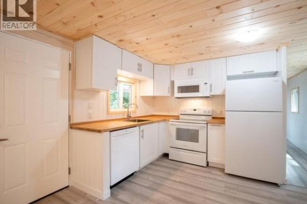 White kitchen with wooden countertops, stainless steel sink, and white appliances including a refrigerator. - 36-6263 Lund, Powell River