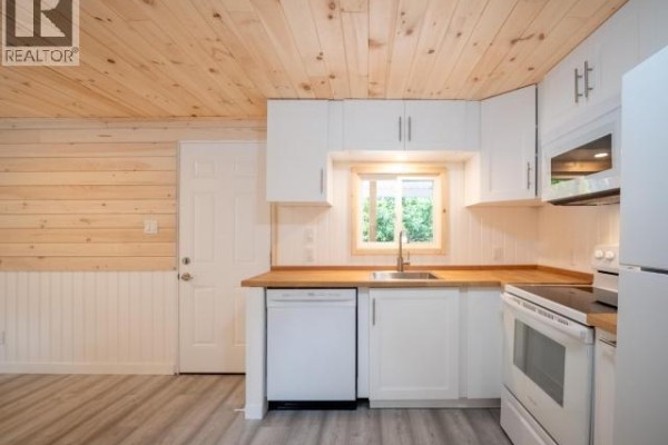 Kitchenette with white cabinets, butcher block counters, white dishwasher, and a window above the sink. - 36-6263 Lund, Powell River